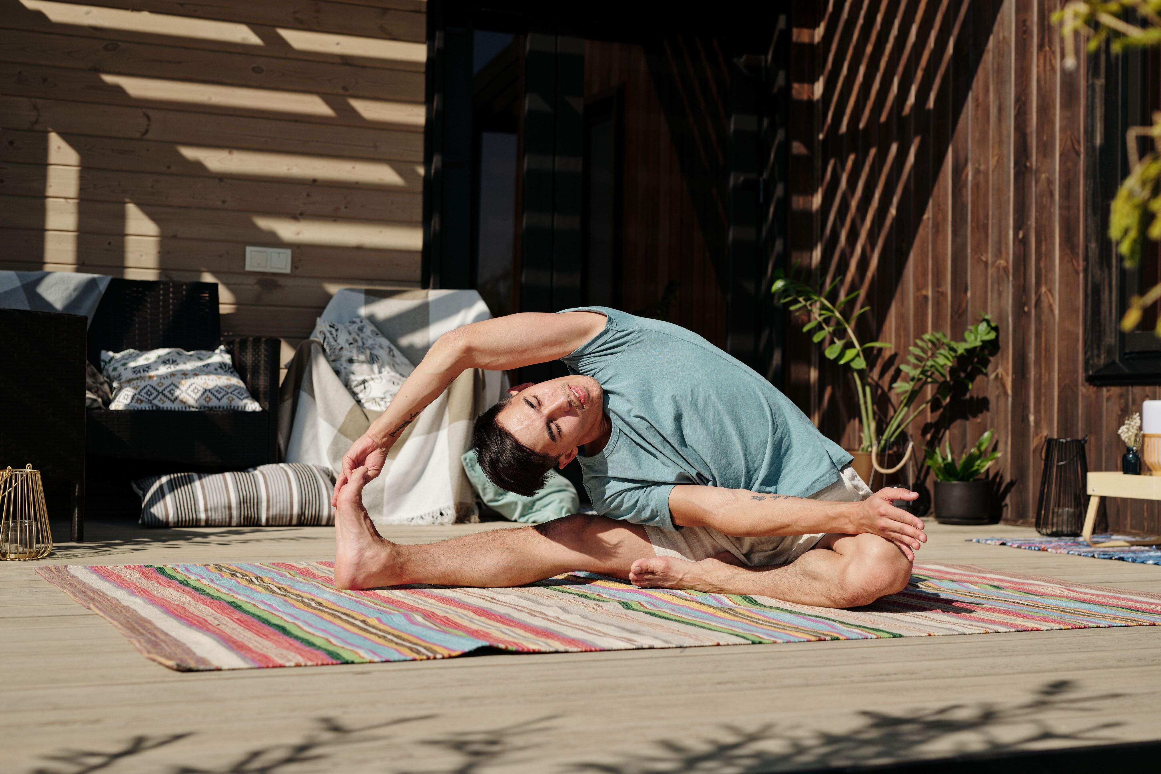Man doing a seated side stretch on a striped mat on a wooden terrace